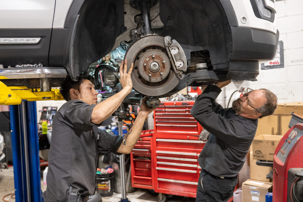 two automotive technicians working on the underside of a car