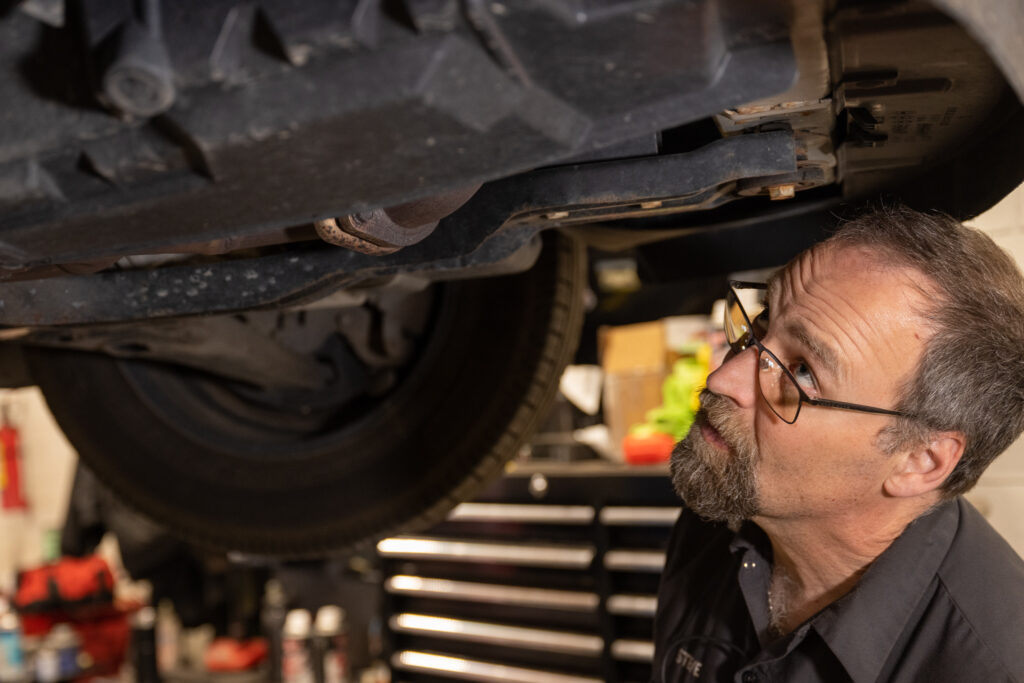 experienced automotive expert looking at the underside of a vehicle and inspecting a car